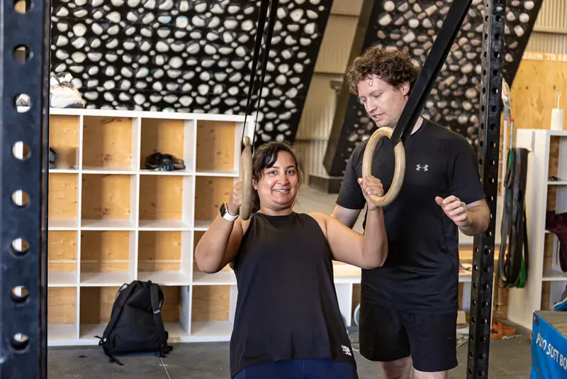 Rick coaching a smiling client through a ring exercise in the gym